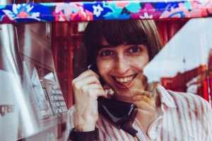 Contact image with a woman holding a phone in a telephone box
