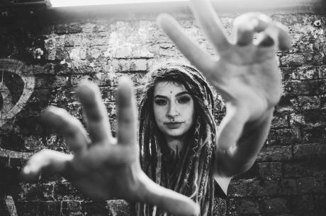 Model with dreadlocks holds out her hands to the camera and frames her face