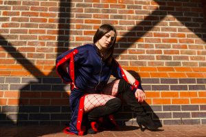 Model knelt in front of brick wall with red popper tracksuit and fishnets