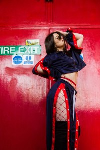 Model holding her face in blue clothes in front of a red door